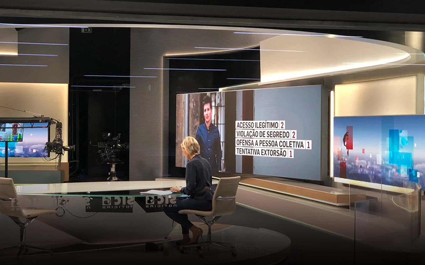 Female news anchor sitting at desk next to multiple video wall graphics